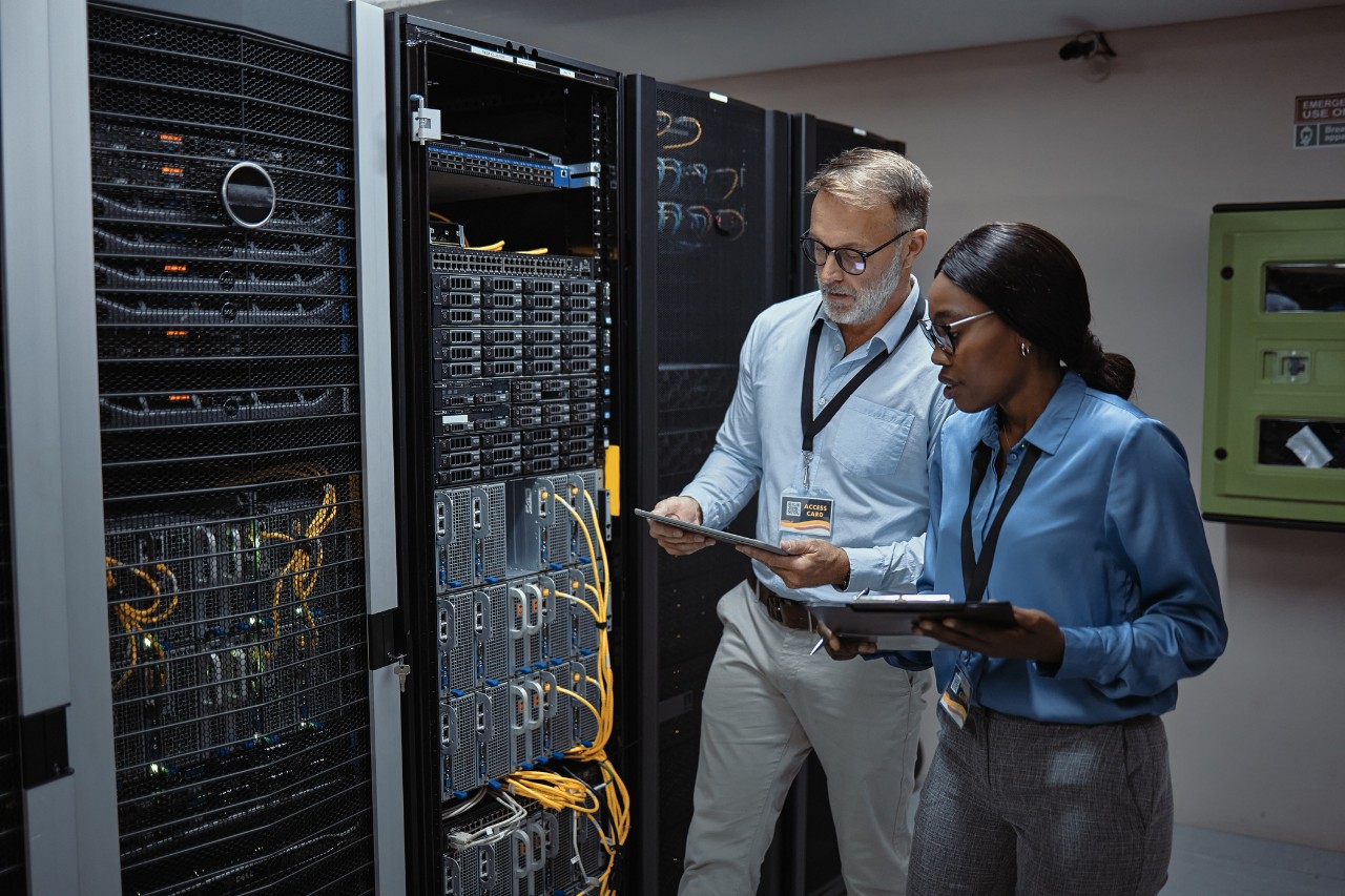 IT technicians using a digital tablet in a server room. Programmers fixing a computer system and network while doing maintenance in a datacenter. Engineers updating security software on a machine