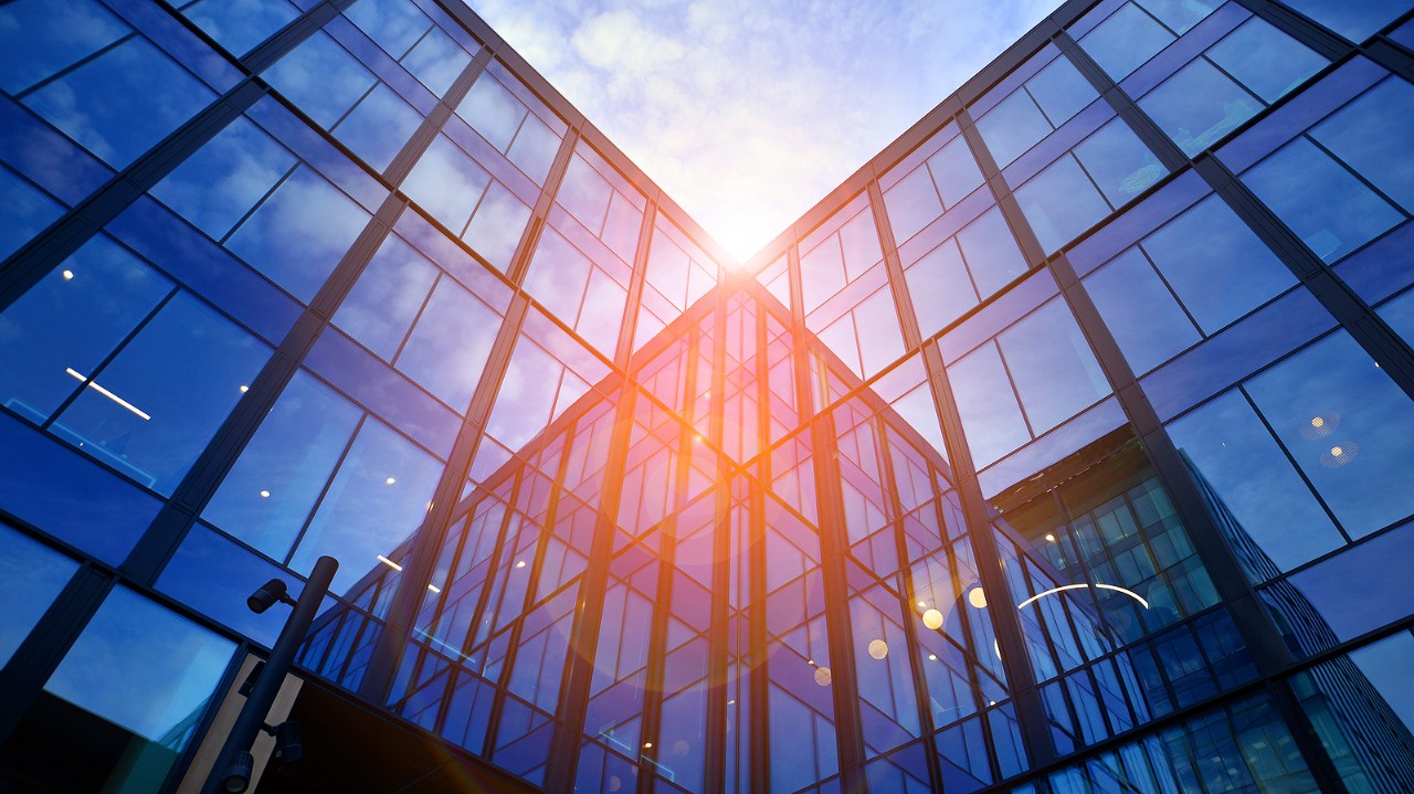 Glass modern building with blue sky background. Low angle view and architecture details. Urban abstract - windows of glass office building in  sunlight day.