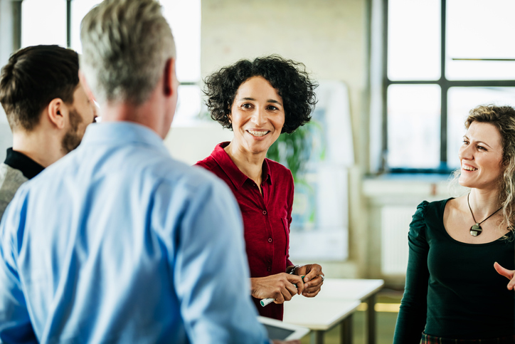 A group of business colleagues standing, having a meeting together in a bright, modern office environment.